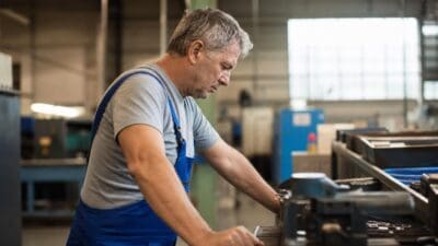 Älterer Arbeiter in blauer Arbeitskleidung bedient Maschine in Fabrikhalle