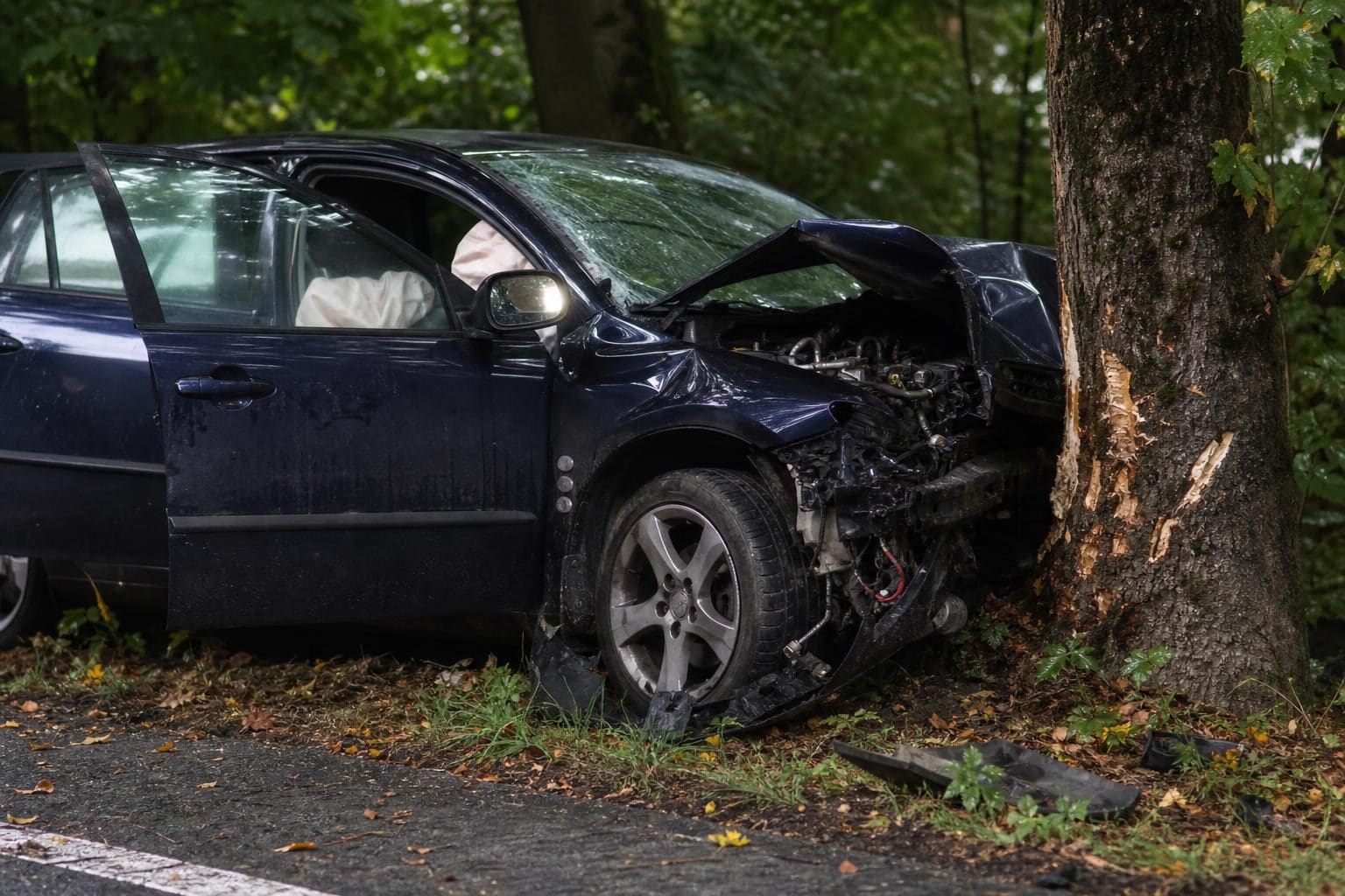 Dunkelblaues Auto mit zerstörter Front gegen Baum geprallt am Waldrand
