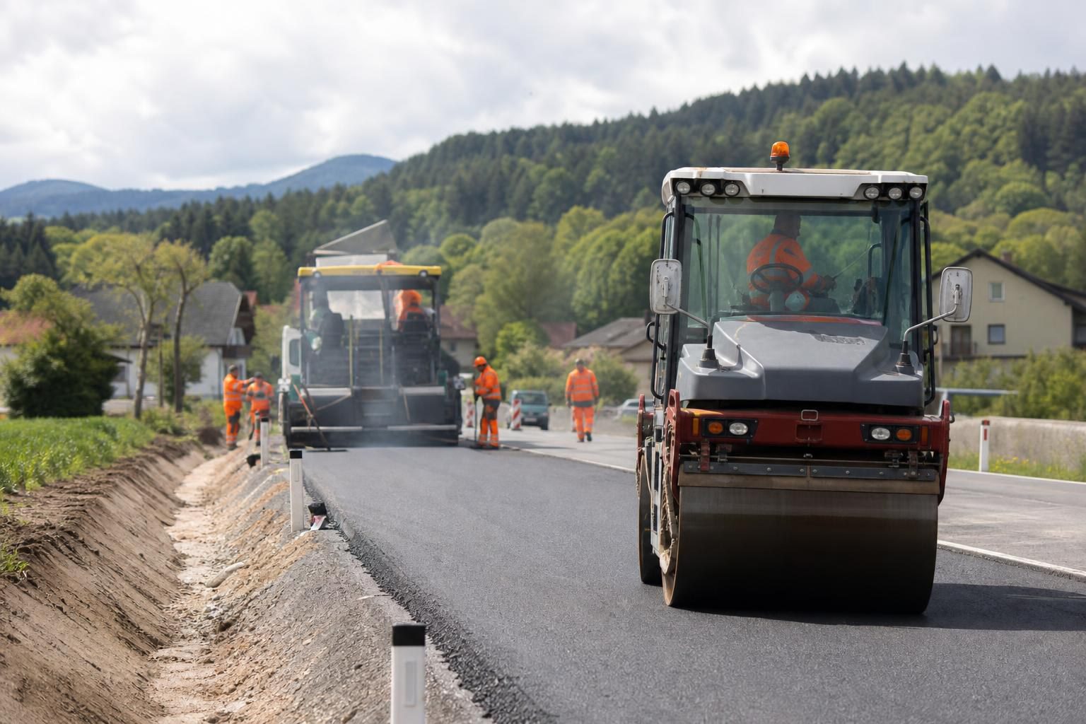 Straßenwalze bei der Asphaltierung einer Landstraße mit Bauarbeitern in Warnwesten