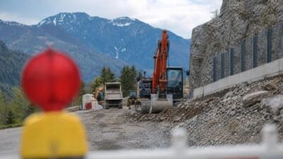 Bagger bei Bauarbeiten auf einer Bergstraße mit Felswand und Bergen