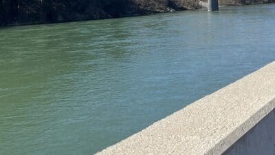 Grünlich schimmernder Fluss mit Betonbrüstung im Vordergrund