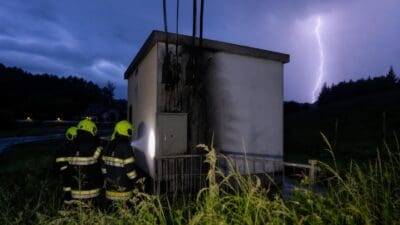 Feuerwehrleute beleuchten mit Taschenlampe eine vom Blitz beschädigte Trafostation bei Nacht