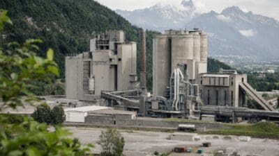 Industrieanlage mit Betonsilos und Schornstein vor bewaldeten Bergen