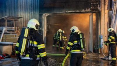 Feuerwehrleute in Schutzkleidung vor verrauchter Halle mit offener Tür bei Nacht