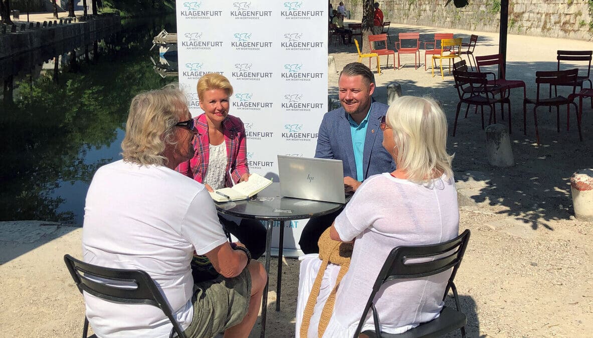 Vier Personen sitzen an einem Tisch im Freien und diskutieren bei einem Sprechtag.