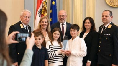 Kinder und Erwachsene posieren mit Glasaward im Landtagssaal vor Fahnen
