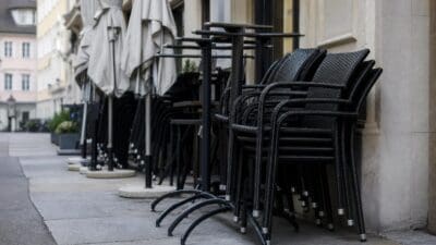 Gestapelte schwarze Stühle und Tische mit geschlossenen Sonnenschirmen auf einem Gehsteig