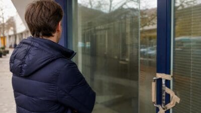 Mann mit braunen Haaren in blauer Daunenjacke steht vor einer Glastür mit abgeklebtem Griff