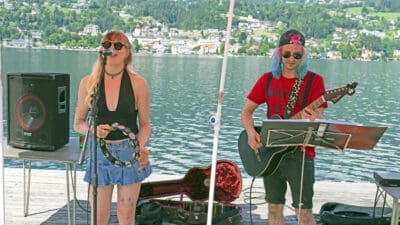 Sängerin mit Mikrofon und Gitarrist auf einer Bühne am Seeufer