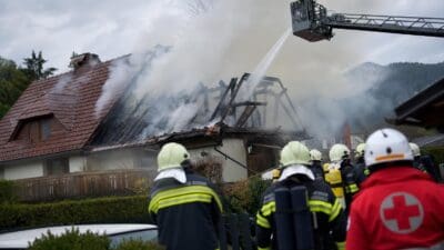 Feuerwehrleute löschen Dachstuhlbrand an Wohnhaus mit Drehleiter und Wasserstrahl
