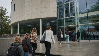 Gruppe junger Menschen mit Rucksäcken betritt modernes Gebäude mit Glasfassade