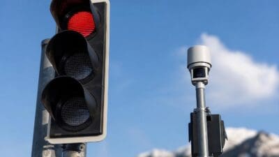 Rote Verkehrsampel neben einer Kamera an einem Pfosten vor blauem Himmel