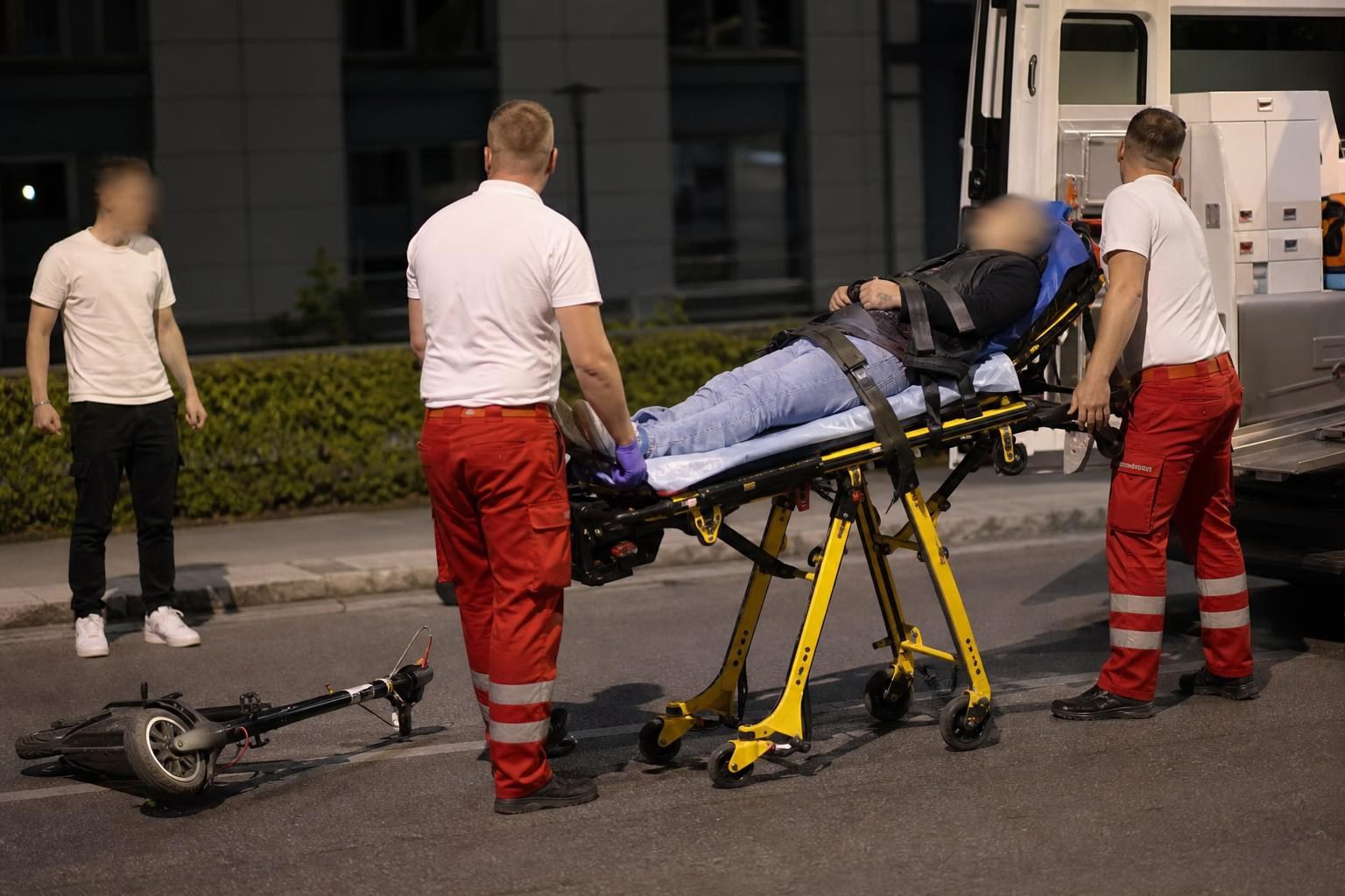 Rettungskräfte schieben verletzten Mann auf Trage in Krankenwagen, E-Scooter liegt auf der Straße