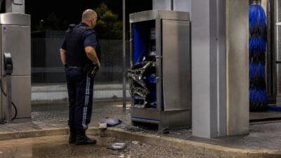 Polizist steht vor einem aufgebrochenen Automaten an einer Autowaschanlage bei Nacht