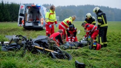Rettungskräfte versorgen verletzten Motorradfahrer neben Unfallmotorrad auf Wiese bei Rainbach