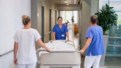 Pflegekräfte schieben ein Krankenbett mit Patient durch einen hellen Klinikflur