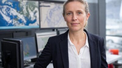 Porträt von Elke Ludewig in einem modernen Wetterüberwachungsbüro mit Bildschirmen im Hintergrund