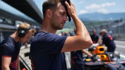 Schweißnasser Rennfahrer wischt sich mit einem Tuch die Stirn vor einem Formel-1-Auto