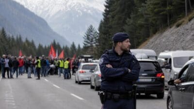 Polizist steht mit verschränkten Armen auf einer gesperrten Straße vor einer Demonstration in den Bergen