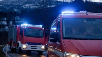 Zwei rote Einsatzfahrzeuge der Feuerwehr mit aktiviertem Blaulicht auf einer Landstraße in den Bergen