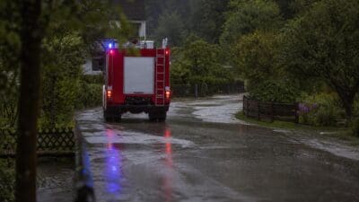 Rotes Feuerwehrauto mit Blaulicht fährt auf nasser Straße davon