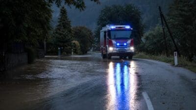 Rotes und weißes Feuerwehrfahrzeug mit Blaulicht auf überfluteter Straße bei Dämmerung