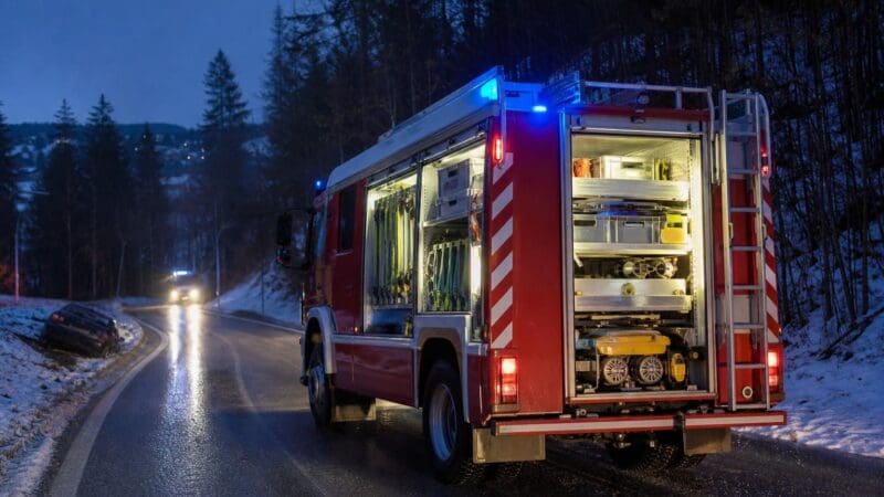 Rotes Feuerwehrfahrzeug mit geöffnetem Geräteraum auf verschneiter Straße bei Nacht