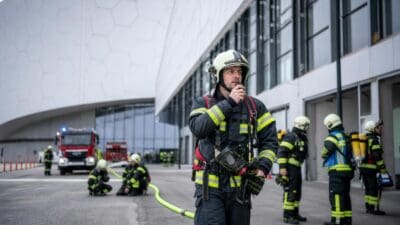 Feuerwehrmänner in Schutzkleidung bei einer Übung vor einem großen Gebäude mit Einsatzfahrzeugen