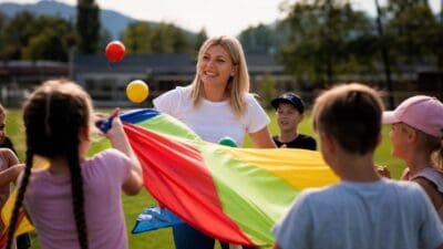 Betreuerin und Kinder halten bunten Spiel Fallschirm auf grüner Wiese