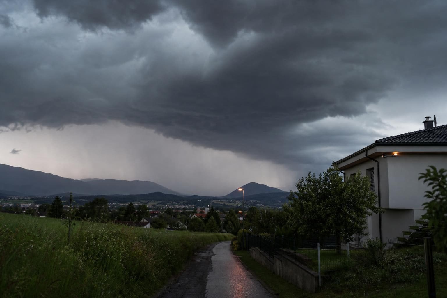 Dunkle Gewitterwolken mit Regenschauern über ländlicher Siedlung und Bergen