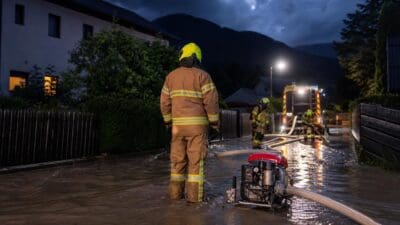 Feuerwehrmänner in Schutzkleidung stehen in einer überfluteten Straße bei Nacht