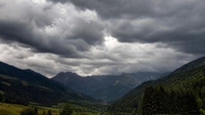 Dunkle Sturmwolken über einem grünen Bergtal mit Wäldern und Bergen