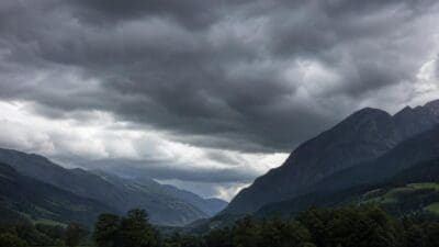 Dunkle Gewitterwolken über grünem Tal mit Bergen und Bäumen