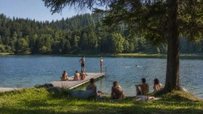 Menschen baden und entspannen am Ufer eines Sees mit Holzsteg und Wald
