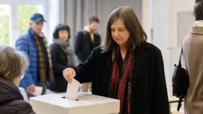 Eine Frau steckt einen Stimmzettel in eine Wahlurne in einem Wahllokal.