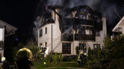 Feuerwehrleute löschen mit Wasserstrahlen einen Brand in einem stark beschädigten Mehrfamilienhaus bei Nacht