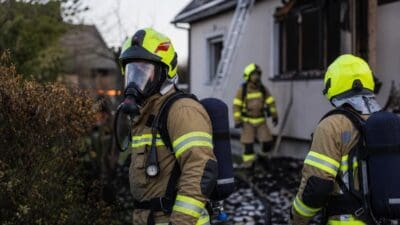 Feuerwehrmänner in Atemschutzgeräten vor einem beschädigten Einfamilienhaus nach einem Brand