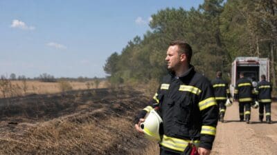 Feuerwehrmann in Uniform hält weißen Helm vor verbranntem Waldboden