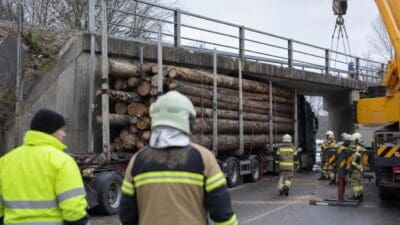 Feuerwehrleute und Kran bergen Holztransporter unter Betonbrücke