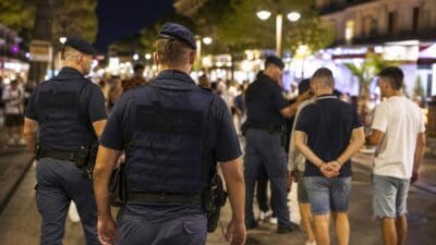Mehrere Polizisten in blauen Uniformen und Schutzwesten stehen nachts auf einer belebten Straße