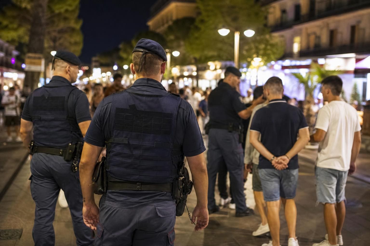 Mehrere Polizisten in blauen Uniformen und Schutzwesten stehen nachts auf einer belebten Straße