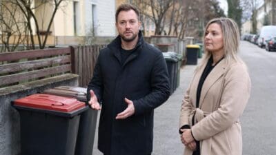 Patrick Jonke gestikuliert neben einer Frau vor Mülltonnen auf einer Straße