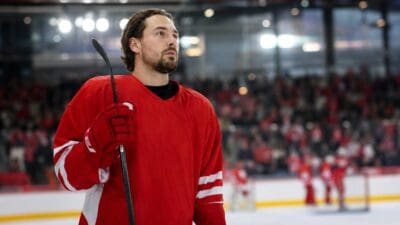 Eishockeyspieler in rotem Trikot hält Schläger auf dem Eis einer Arena