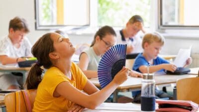 Schülerin in gelbem Shirt kühlt sich mit Fächer im Klassenzimmer ab