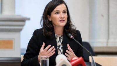 Eine Frau mit dunklen Haaren gestikuliert bei einer Pressekonferenz am Tisch sitzend.