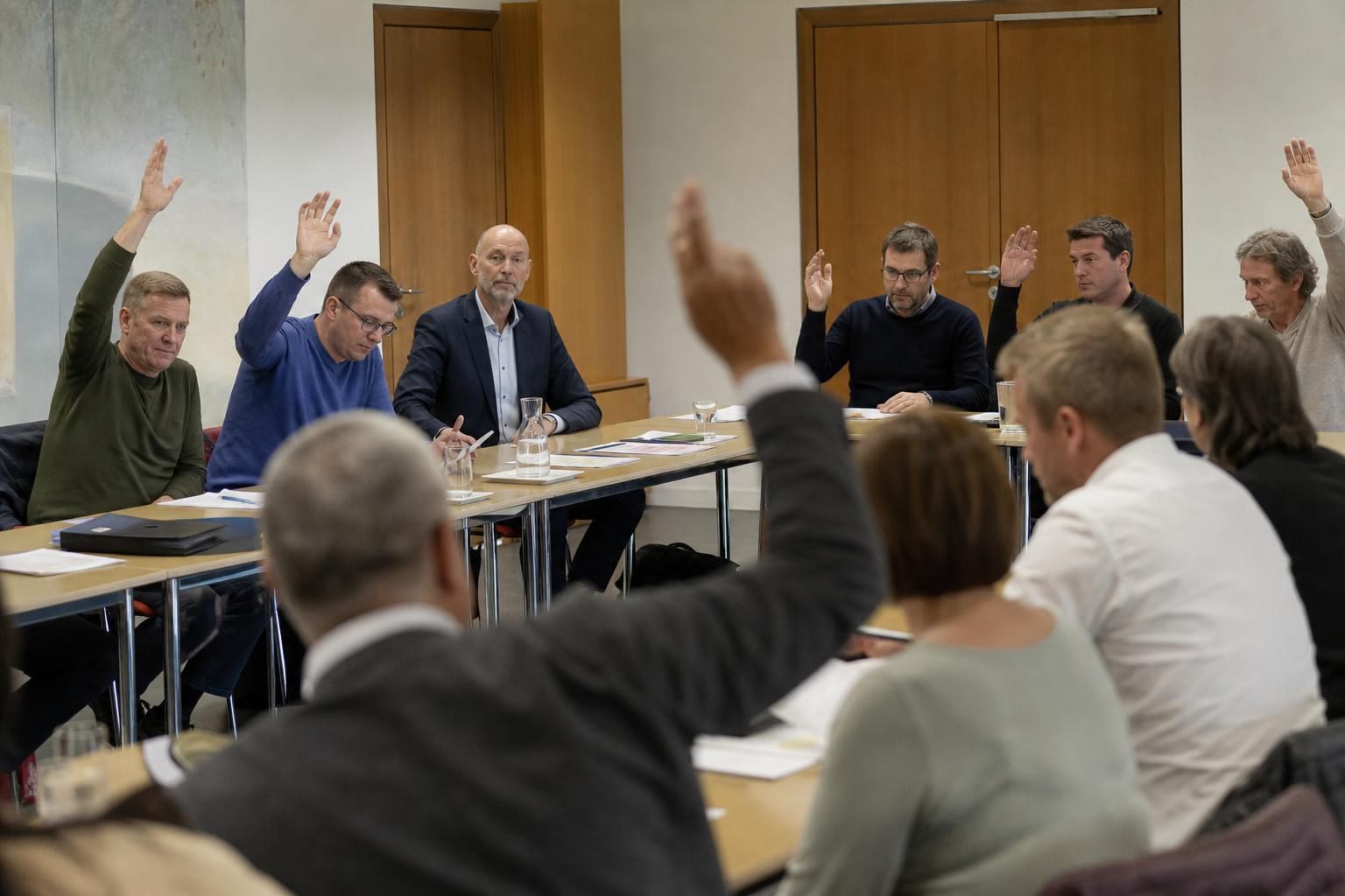 Mehrere Personen an einem Tisch heben die Hand zur Abstimmung.