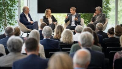 Vier Personen diskutieren auf einer Bühne vor einem Publikum in einem hellen Saal