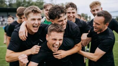 Junge Fußballspieler in schwarzen Trikots jubeln gemeinsam auf dem grünen Rasen