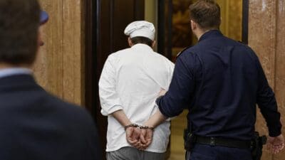 Polizist führt einen in Handschellen gefesselten Koch in ein Gebäude