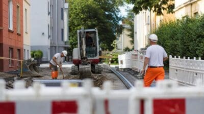 Bauarbeiter und Bagger bei Grabungsarbeiten in einer gesperrten Straße mit Absperrungen